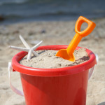 Child's beach bucket full of sand on a beach.  Medium-shallow focus on starfish in bucket.